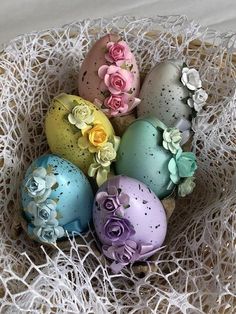 an arrangement of colorful decorated eggs in a basket on top of white netting with pink, yellow and blue flowers