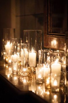 many lit candles are lined up on a long table with glass vases and glasses