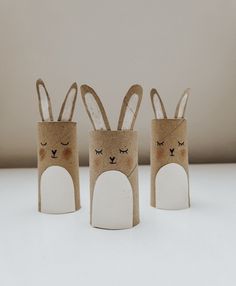 three toilet paper roll rabbits with eyes and ears on them, standing in front of a white wall