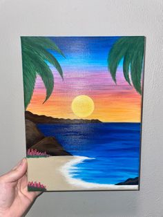 a person holding up a piece of art that is painted with palm trees on the beach