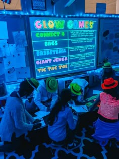 children are sitting at desks in front of a large sign that says glow games