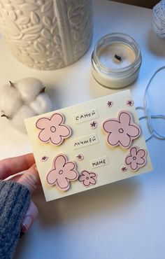 a person is holding up a card with flowers on it next to yarn and cotton balls