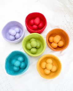 four bowls filled with different colored balls on a white tablecloth, one has an egg in the middle