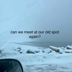 a car driving down a snow covered road next to the ocean with an overcast sky