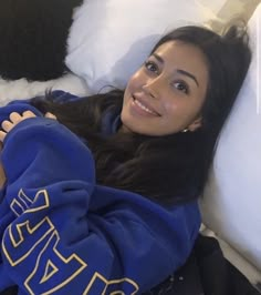 a woman laying on top of a bed wearing a blue sweatshirt and smiling at the camera