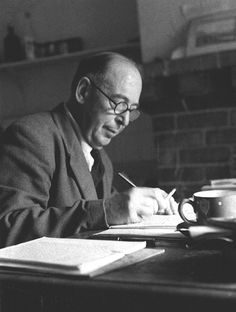 a man sitting at a table writing in a book with a cup on top of it