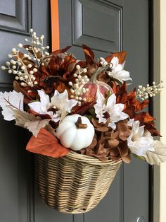 a basket filled with white pumpkins and fall leaves hanging on a door handle next to a gray front door