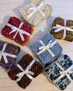 six knitted gift boxes with white ribbons and bows on the top, all in different colors