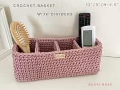 a pink knitted basket with two cell phones and a hair brush in it next to a white wall