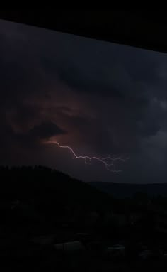 a lightning bolt is seen in the sky over a city at night with dark clouds