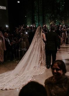 the bride is walking down the aisle with her veil draped over her head and she is surrounded by people