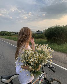 a girl is riding her bike down the road with flowers in front of her face