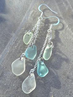 three sea glass dangles are hanging from silver chain earwires on the sand