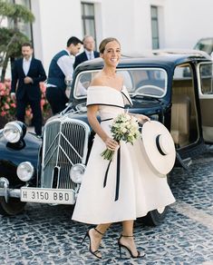 a woman in a white dress standing next to an old car