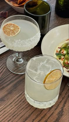 two glasses filled with drinks sitting on top of a table next to plates and utensils