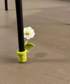 a crocheted flower in a yellow vase on the ground next to a black pole