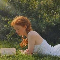 a woman laying in the grass reading a book