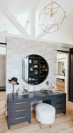 a room with a desk, mirror and stools in front of the wall that has a large circular mirror on it