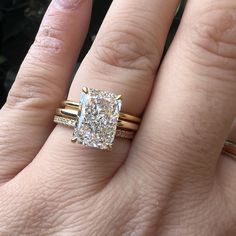 a woman's hand with two gold rings and a cushion shaped diamond ring on it