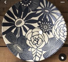 a black and white plate with flowers painted on the front is sitting on a wooden table