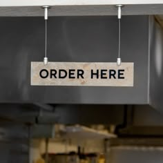 a sign that says order here hanging from the ceiling in a restaurant or cafe kitchen