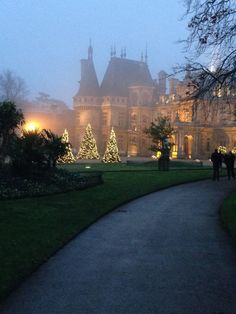 people walking down a path in front of a large building with christmas lights on it