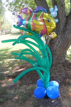 a fish balloon sitting on top of a tree next to some blue and green balloons