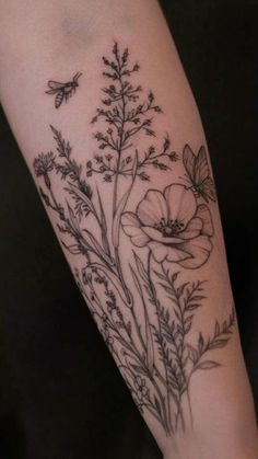 a woman's arm with flowers on it and a bee flying over the top