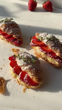 three pastries with strawberries and powdered sugar on them sitting on a white surface