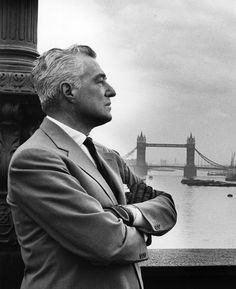 a man standing in front of a bridge with his arms crossed and looking off into the distance