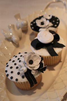 three cupcakes decorated with black and white decorations on a plate, one has a bow