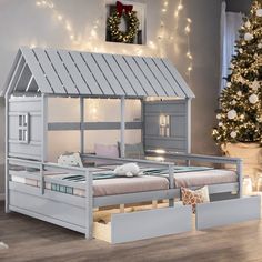 a child's bed with a house on the top and drawers underneath it in front of a christmas tree