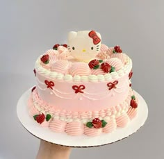 a hello kitty cake on a white plate with pink icing and strawberry decorations,