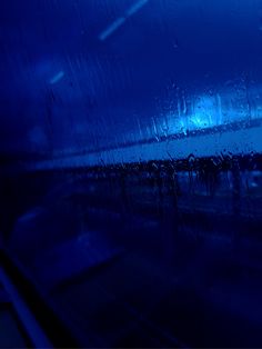 rain drops on the windshield of a car at night time with blue lights in the background