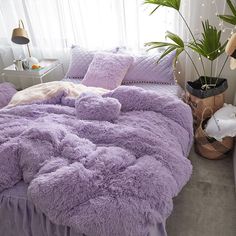 a bed with purple comforter and pillows in a bedroom next to a plant on the floor