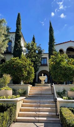 the stairs lead up to an elegant house with trees and bushes on both sides, in front of a blue sky