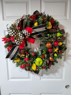 a christmas wreath with apples, pine cones and other holiday decorations hanging on a door