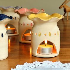 small ceramic vases with candles in them on a wooden table next to a doily