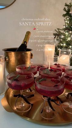 there are many glasses on the tray with wine and candles in front of the christmas tree