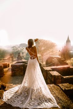 a woman standing on top of a stone wall wearing a white dress and looking at the sky