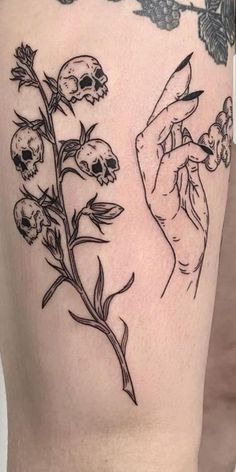 a woman's thigh with skulls and flowers on the side, as well as a hand holding a flower