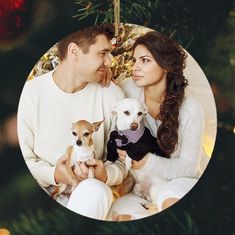 a man and woman sitting next to each other holding small dogs in front of a christmas tree