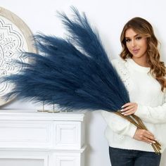 a woman is holding some blue feathers in her hands and looking at the camera while standing next to a fireplace