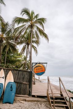 two surfboards are sitting on the beach next to some palm trees and a sign