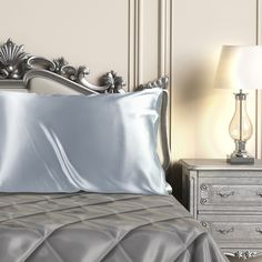 a bed with silver sheets and pillows next to a night stand