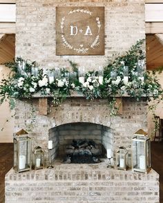 a brick fireplace with candles and greenery on the mantle is decorated with white flowers