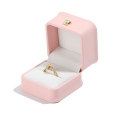 an open pink ring box with a gold wedding band in the middle and a diamond on top