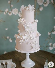 a three tiered pink cake with white flowers on top and silverware next to it