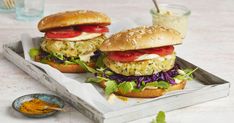 two burgers with lettuce, tomato and onion on a tray next to some dipping sauce