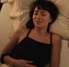 a woman laying in bed with her head on the pillow and eyes closed, smiling